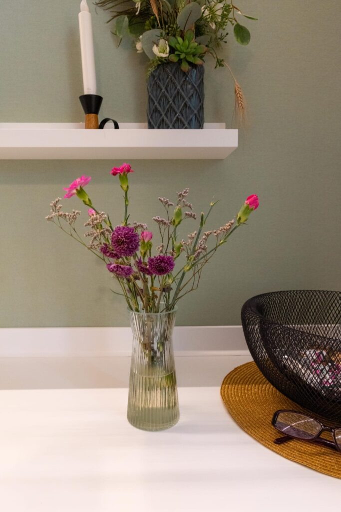 Blumenstrauß in einer Glasvase auf einem Tisch vor einer grünen Wand