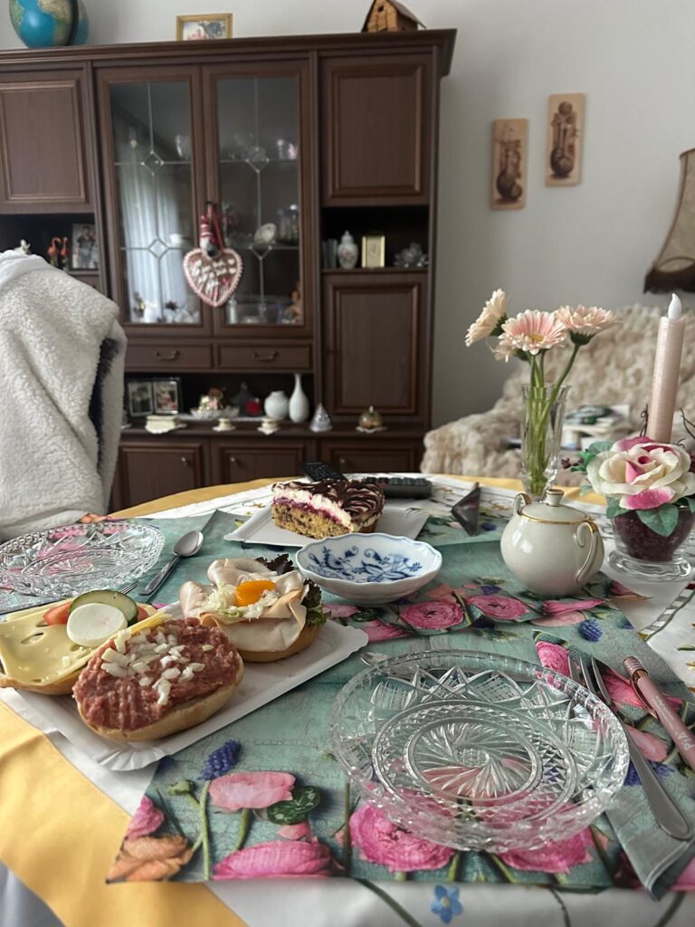 Gedeckter Tisch mit belegten Brötchen, Kuchen und Blumen in einem Wohnzimmer