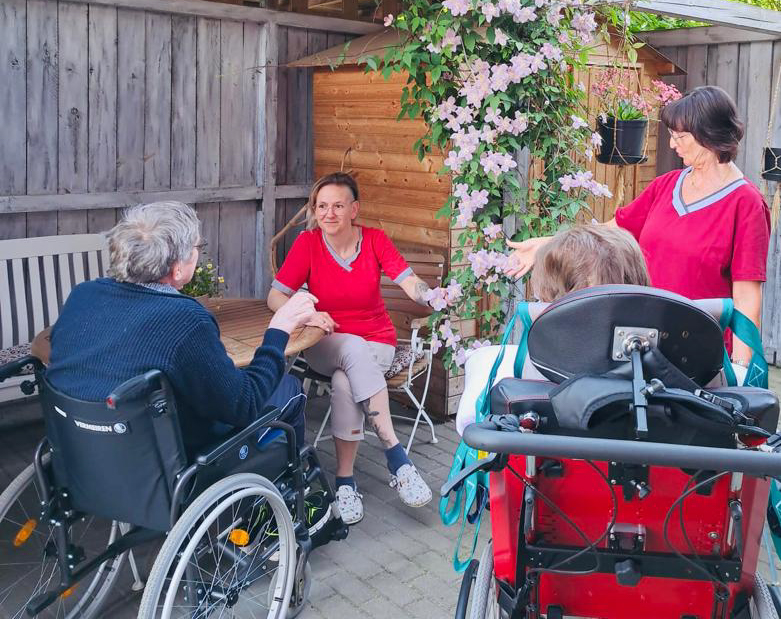 Kunden und Pflegefachkräfte verbringen gemeinsam Zeit im Garten einer Intensivpflege-Wohngemeinschaft